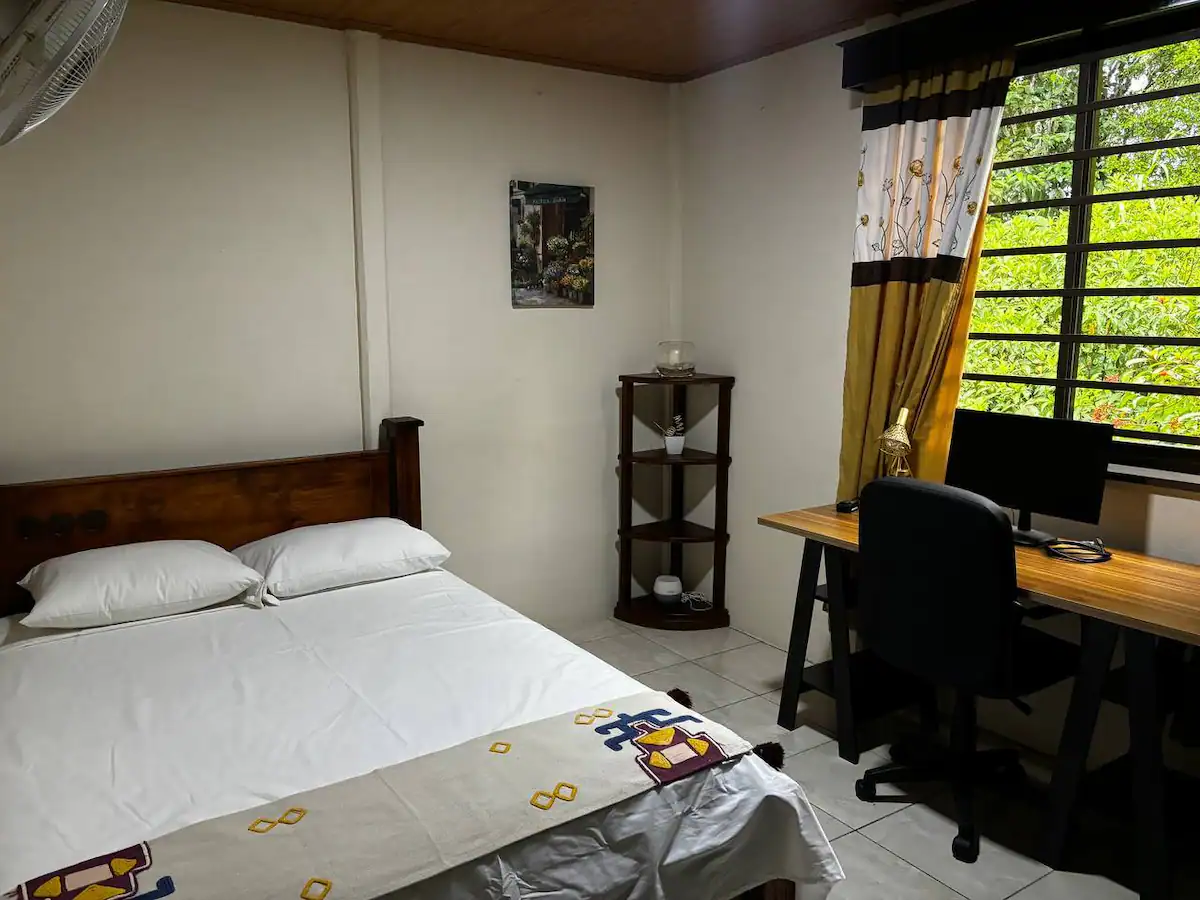 Habitación espaciosa con cama matrimonial, escritorio de trabajo y monitor